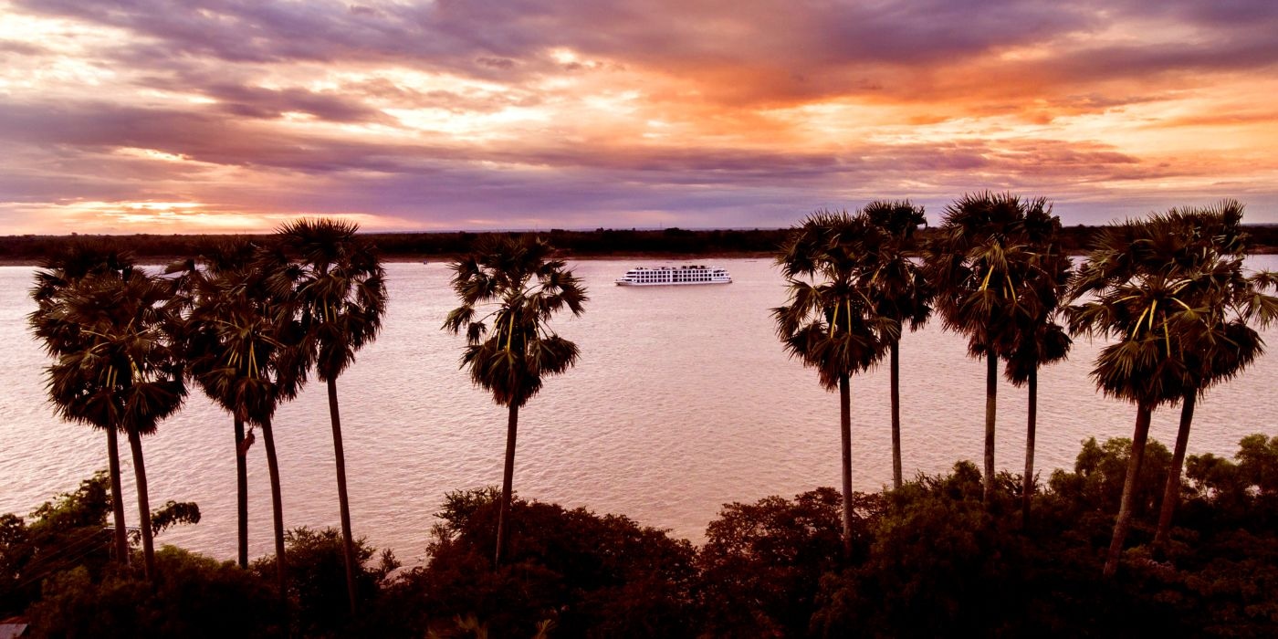 Scenic Spirit can be seen sailing along the Mekong. The sun can be seen setting in the background