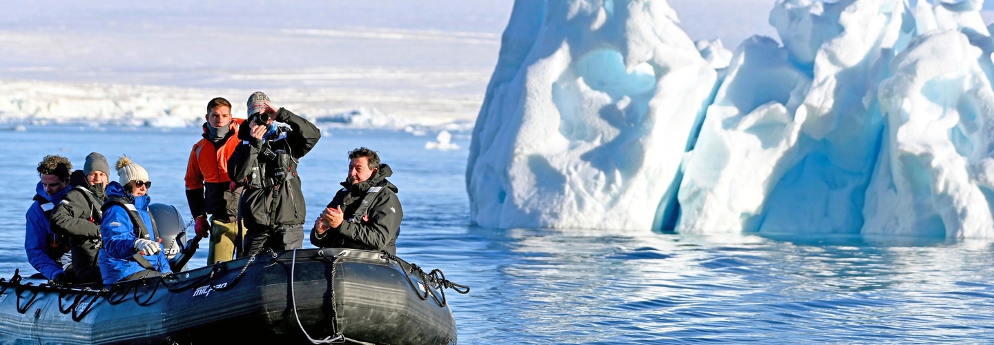 Guests in a Scenic Zodiac exploring icy waters beside a towering blue iceberg